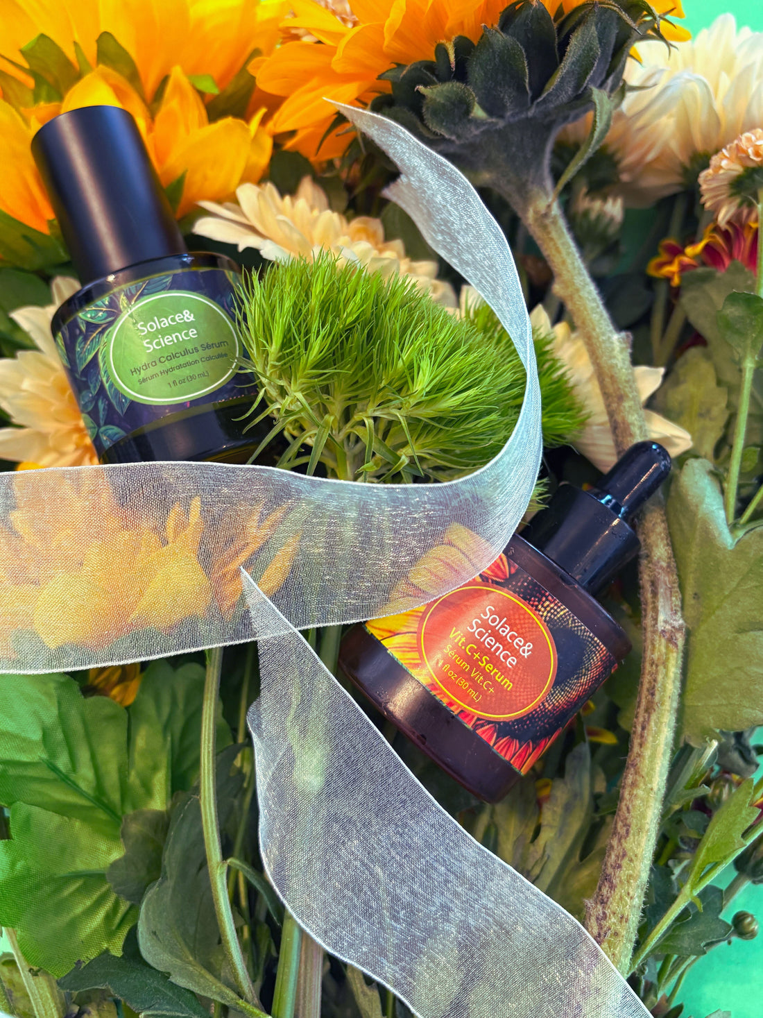 Hydra calculus serum and vitamin c+ serum amid flowers and plants and a transluscent white ribbon
